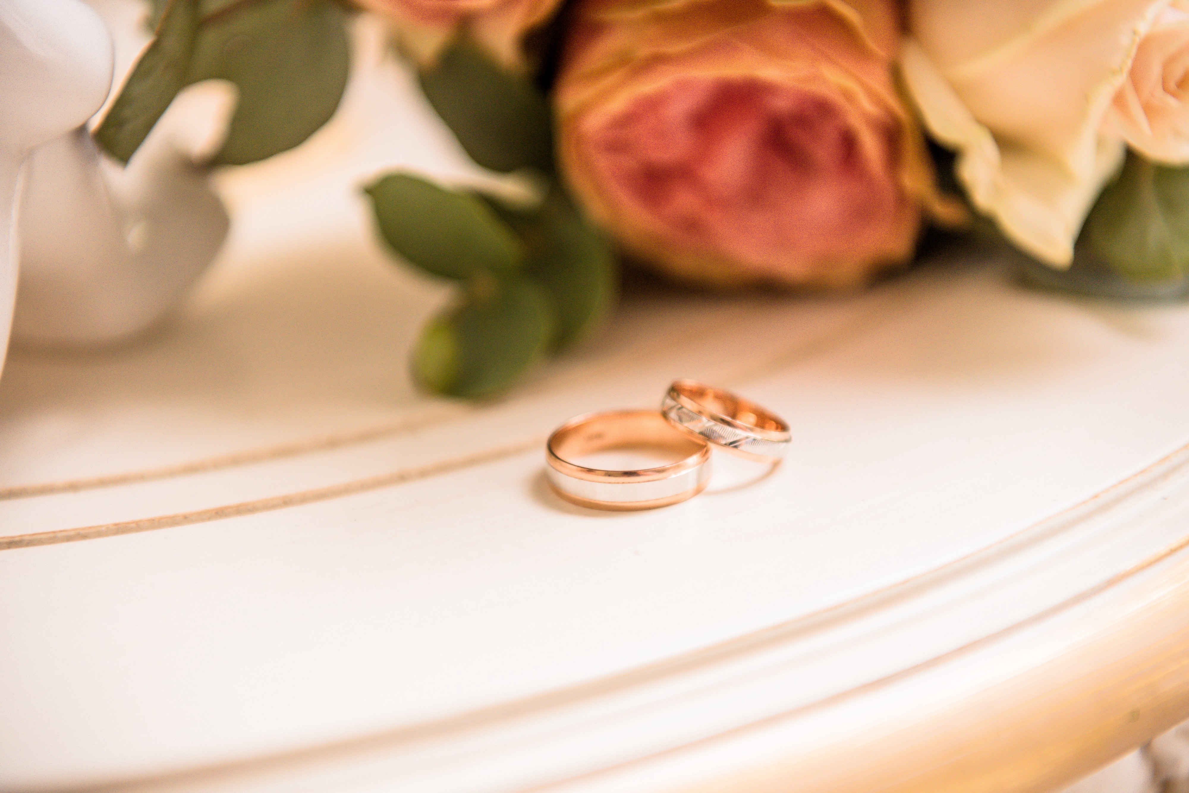 Dois anéis de casamento na mesa com rosas no fundo.