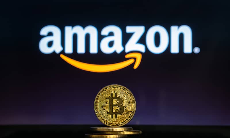 Amazon logo with a stack of physical Bitcoin in front of it.