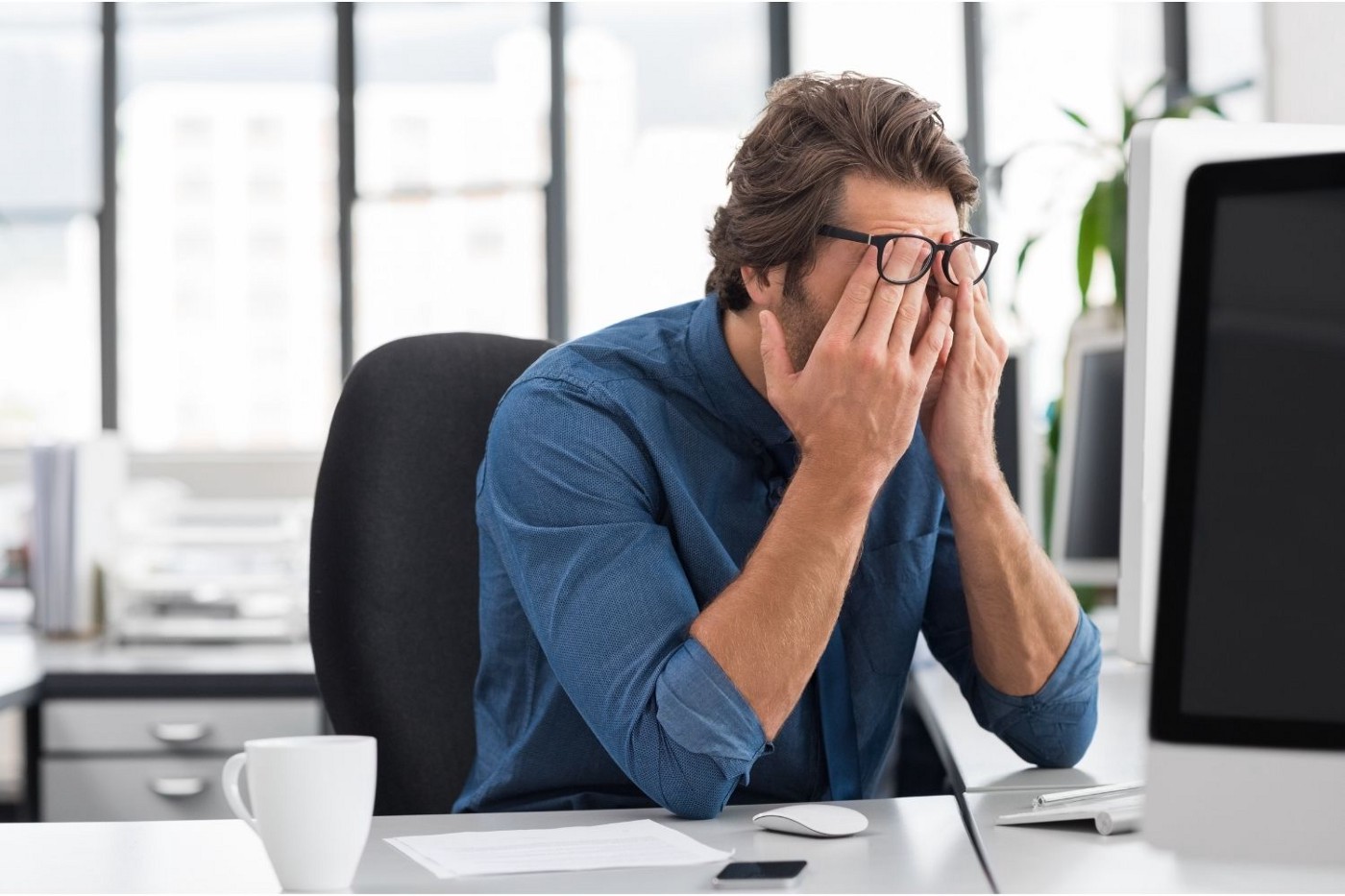 एक तनावग्रस्त व्यक्ति अपने सिर पर हाथ रखकर कंप्यूटर पर बैठा है।