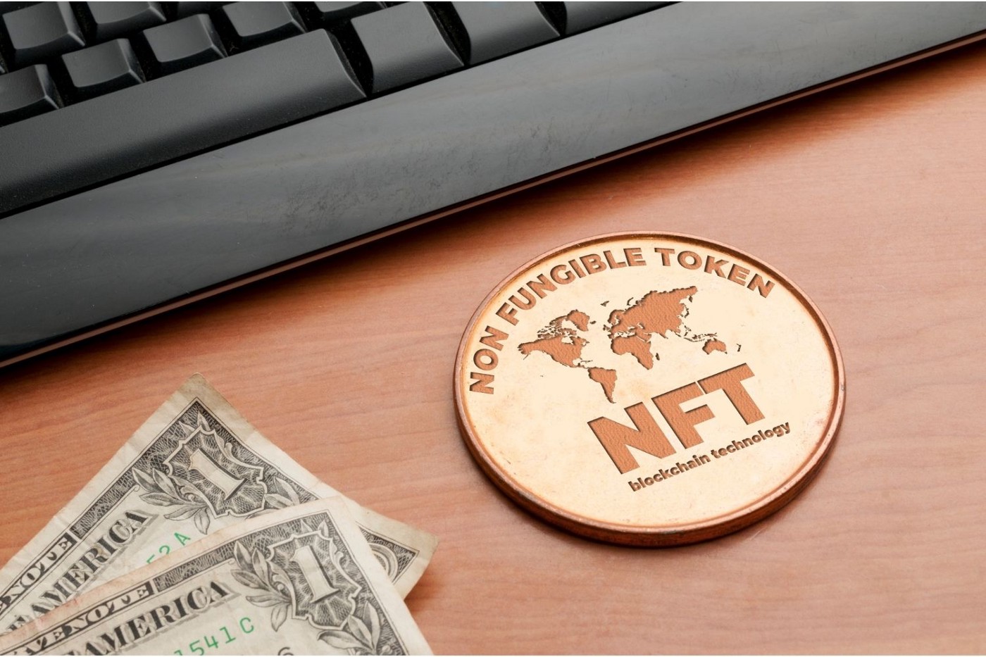 Representasi fisik token NFT yang diletakkan di atas meja dekat keyboard komputer dan dua lembar uang satu dolar.