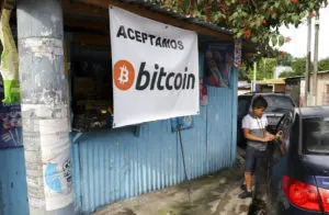En ungdom står ved siden av en bil mens han venter foran en liten butikk som tar imot Bitcoin i San Salvador, El Salvador, lørdag 4. september 2021. Fra og med tirsdag 7. september må alle virksomheter godta betalinger i Bitcoin , bortsett fra de som mangler teknologien til å gjøre det. (AP Photo/Salvador Melendez)