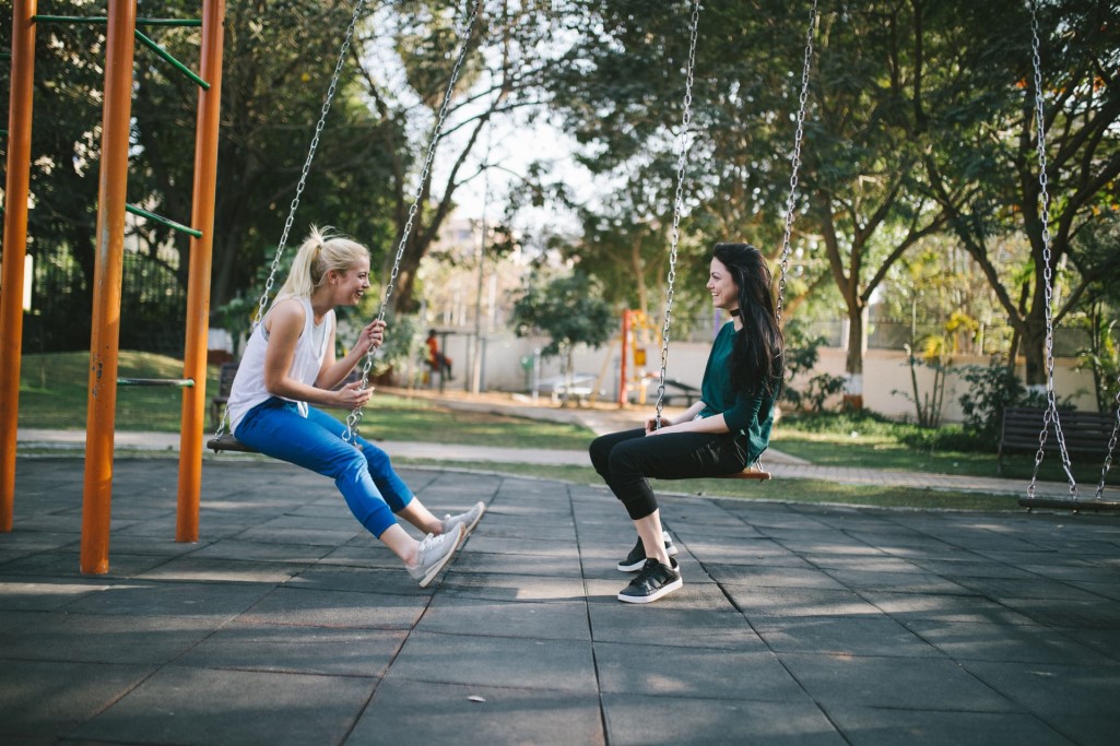 Two women on swings facing each other and smiling