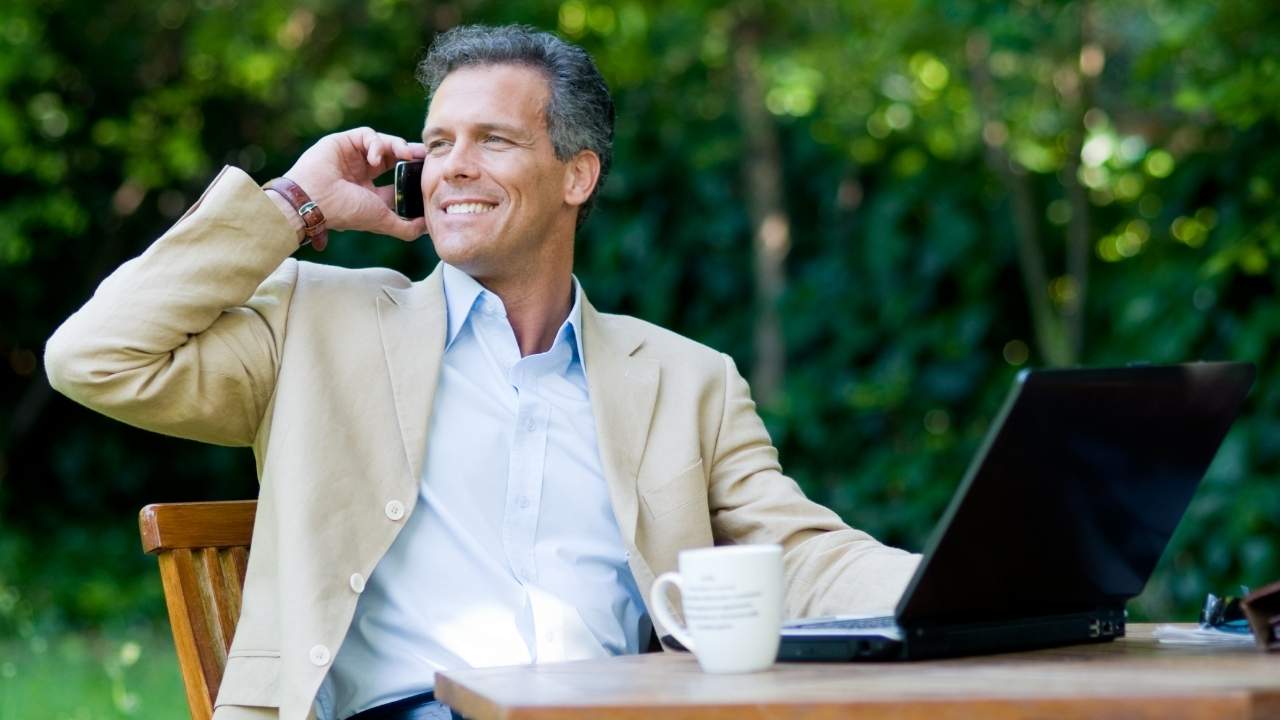 Happy businessman working outdoors with mobile and laptop
