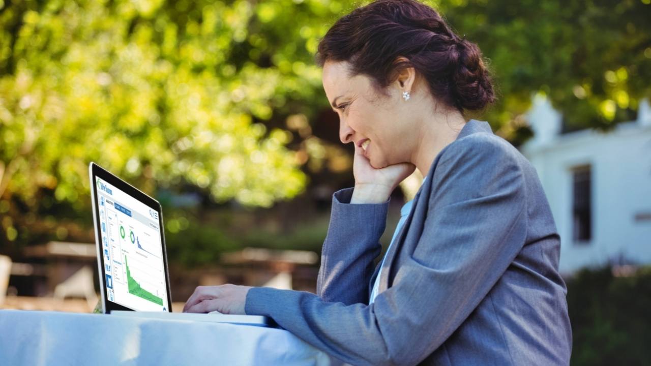 Smiling businesswoman looking over reports on laptop screen outdoors