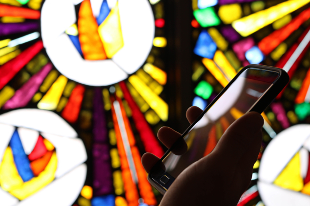 A smartphone held in front of a bright colourful stained glass window
