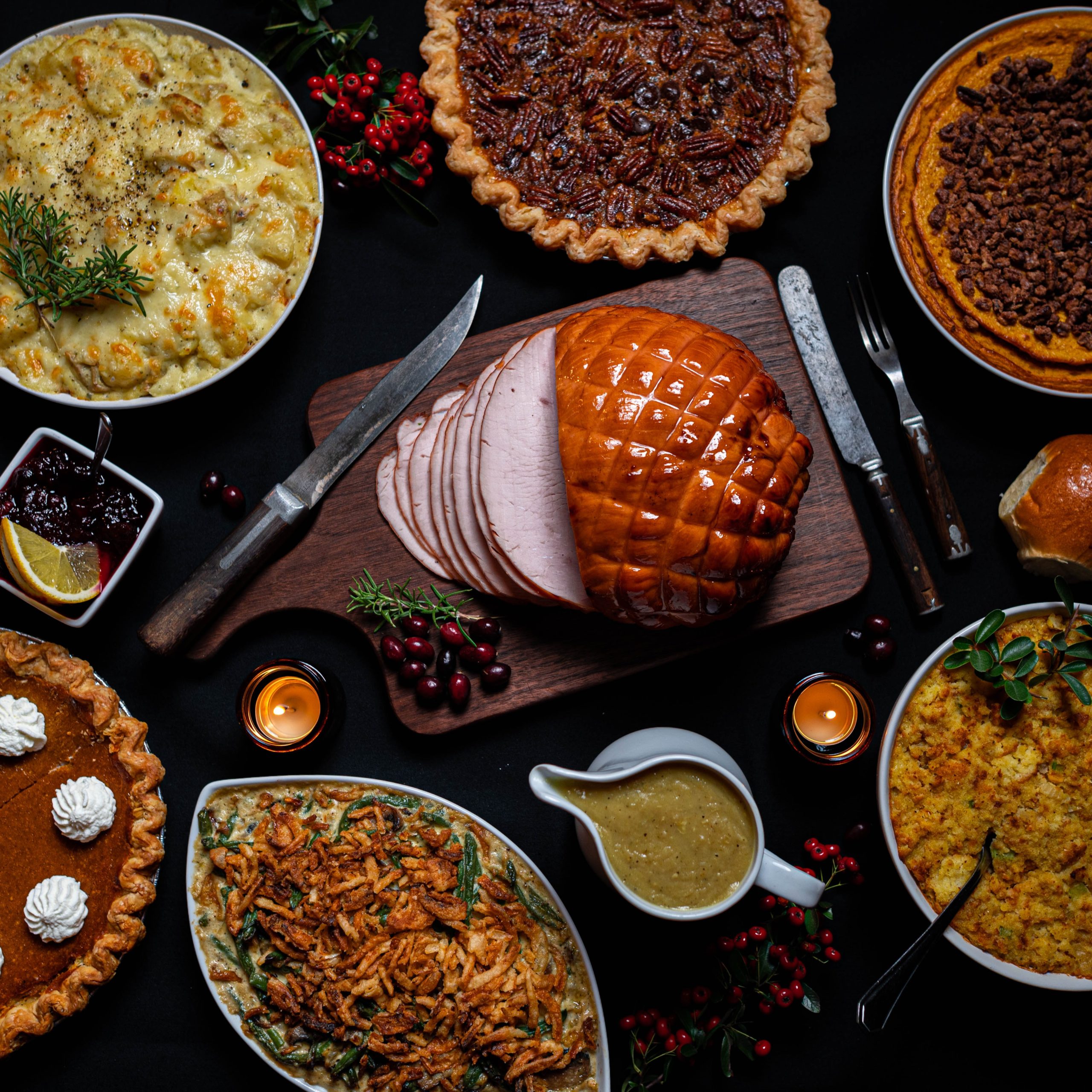 感謝祭の募金活動のアイデア。 艶をかけられたハム、クランベリーソース、ピーカンパイ、パンプキンパイ、グレービー、マック、チーズ、野菜などの感謝祭の食べ物でいっぱいのテーブル