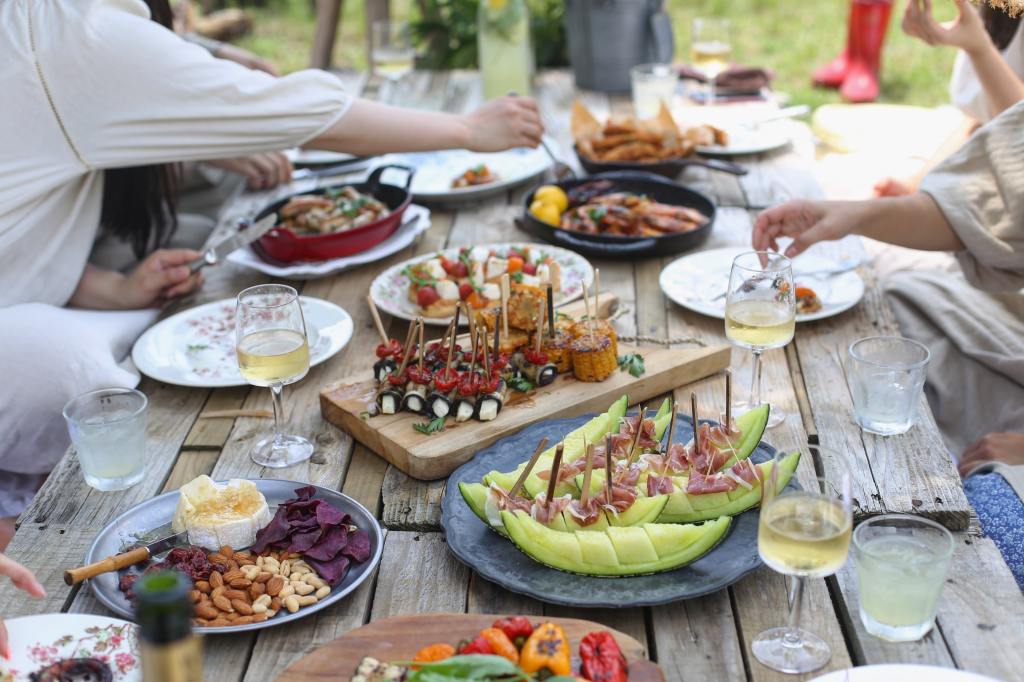 meze, meyve, şarap, peynir ve kuruyemiş içeren bir brunch keyfi yaşayan insanlar