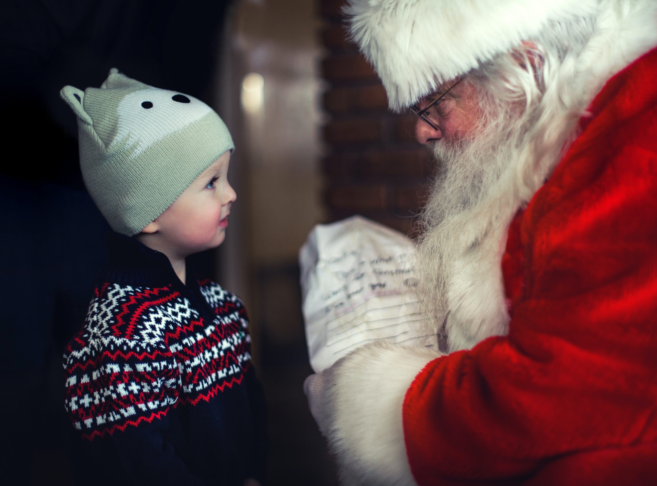 سیاہ سویٹر میں چھوٹا بچہ سانتا کلاز کے سامنے کھڑا ہے۔
