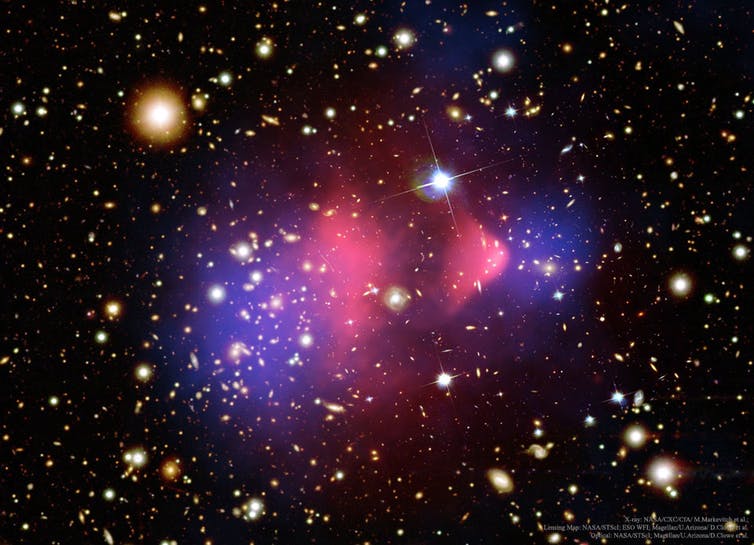 Galaksijoukko vaaleanpunaisen ja violetin sävyinä mustaa kosmista taustaa vasten.