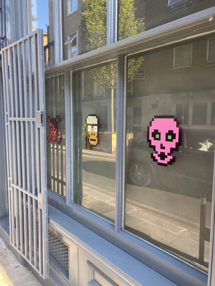 ایک دکان کے باہر رنگت والی کھڑکیوں اور Ape CryptoPunk NFT اور ایک Cryptoskull NFT کی تصاویر۔