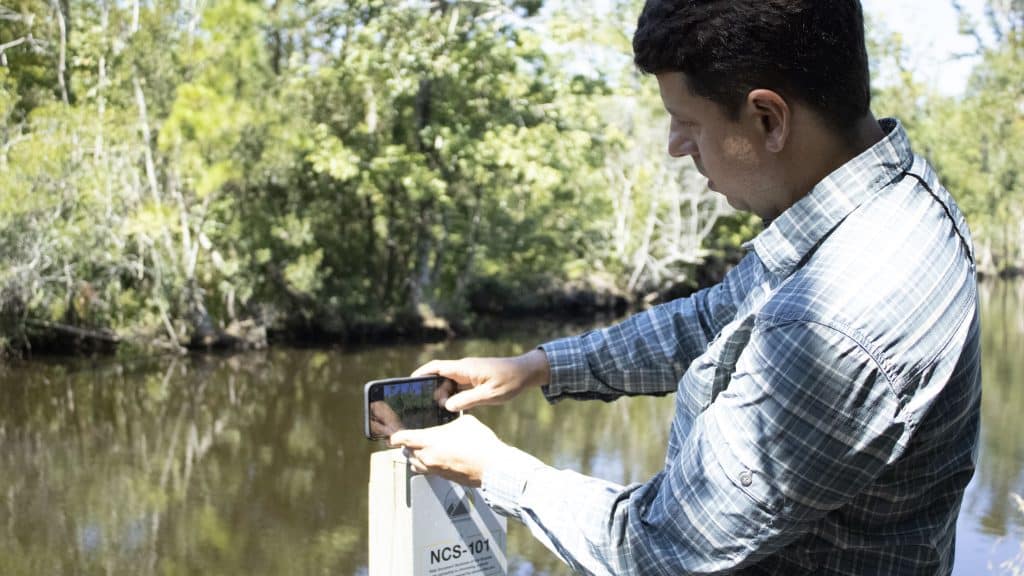 أحد الباحثين في ولاية نورث كارولاينا يوضح استخدام محطة علمية للمواطنين لالتقاط صورة لغابة.