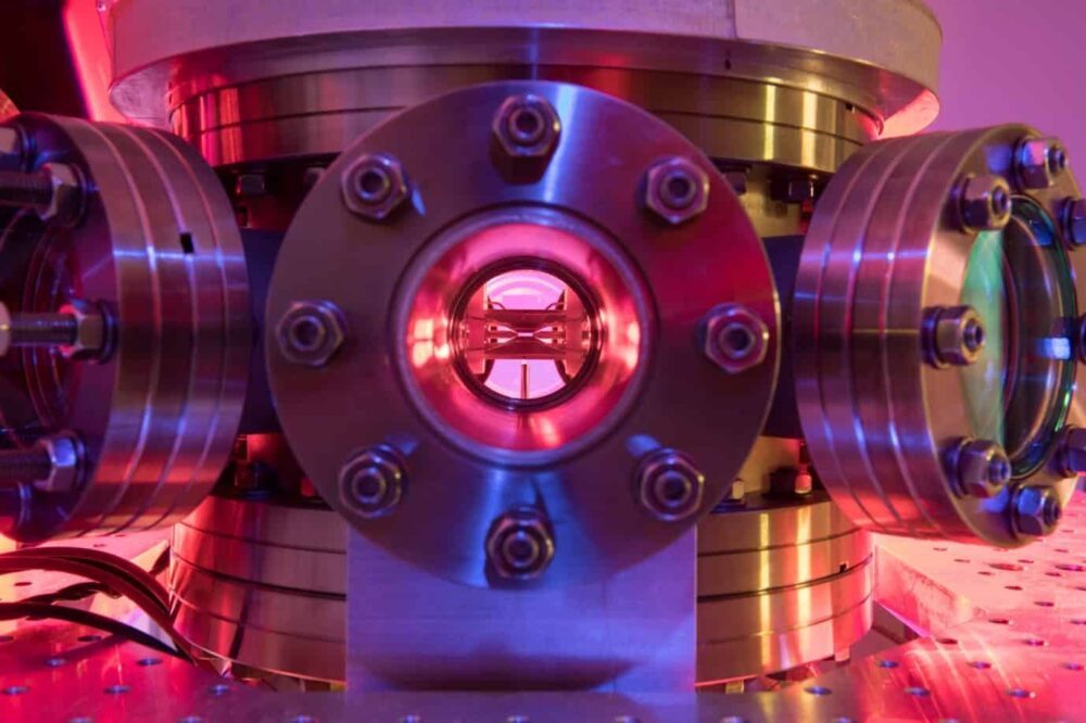 Photo of the ion trap used in the experiment, viewed through a port in a vacuum chamber and bathed in pink light