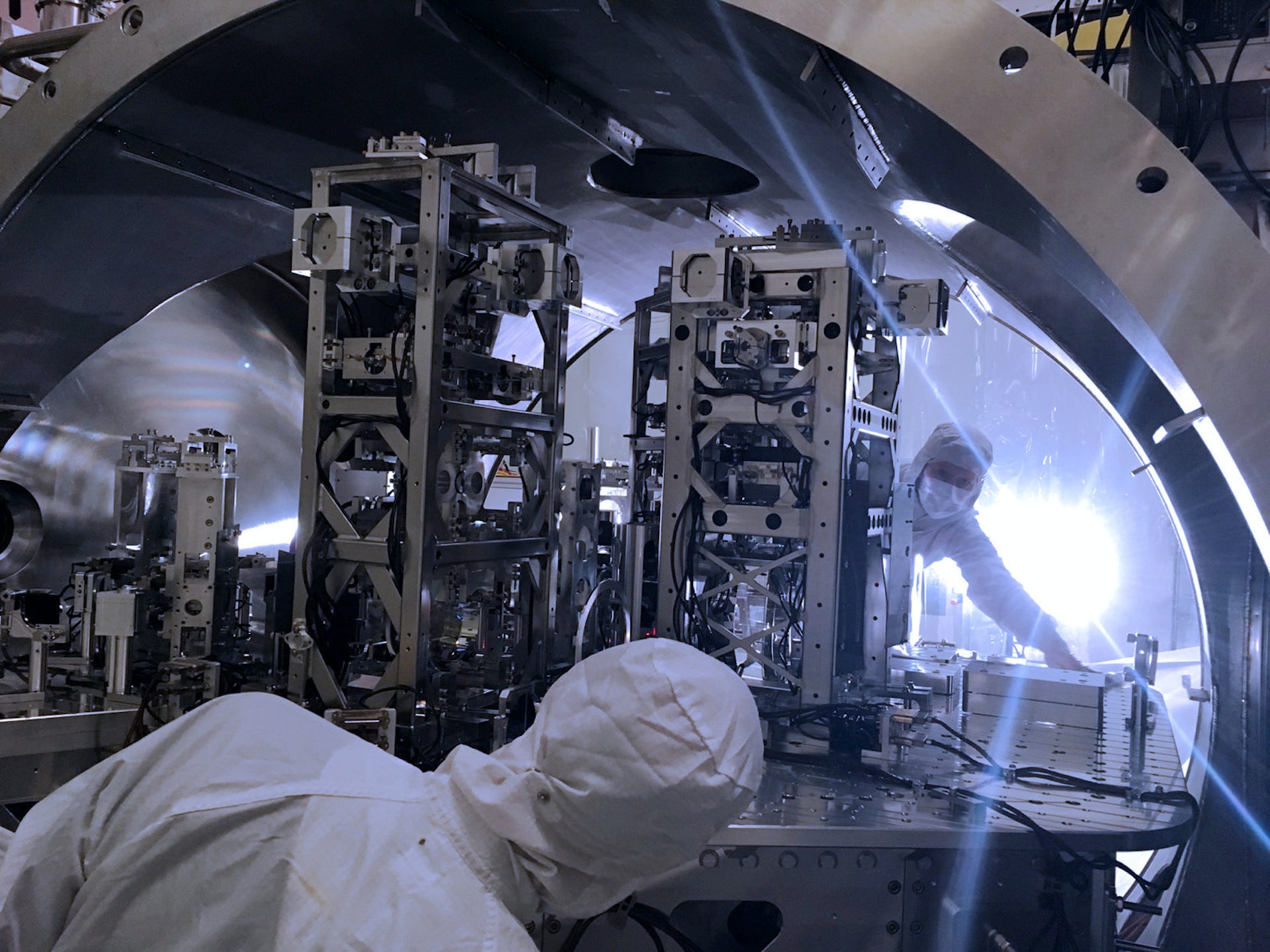 Karmaşık makineler üzerinde çalışan beyaz laboratuvar kıyafetleri içindeki iki kişi.