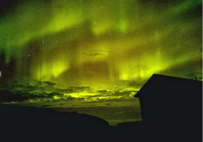 Die Aurora Borealis oder Nordlichter füllen den Nachthimmel über der Silhouette eines Hauses.