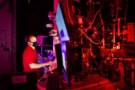 Foto Ryan Schoell sedang melihat layar komputer di laboratorium gelap yang bermandikan sinar laser merah