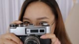 En kvindelig fotograf iført briller og holder et kamera