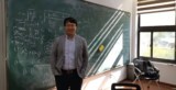 Photo of Wei Li standing in front of a blackboard