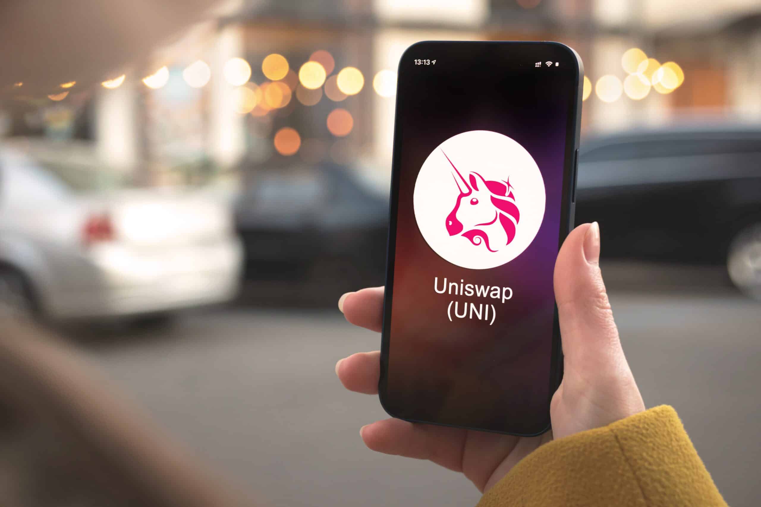 Uniswaps logo af en pink enhjørning vises på en telefon i en persons hånd