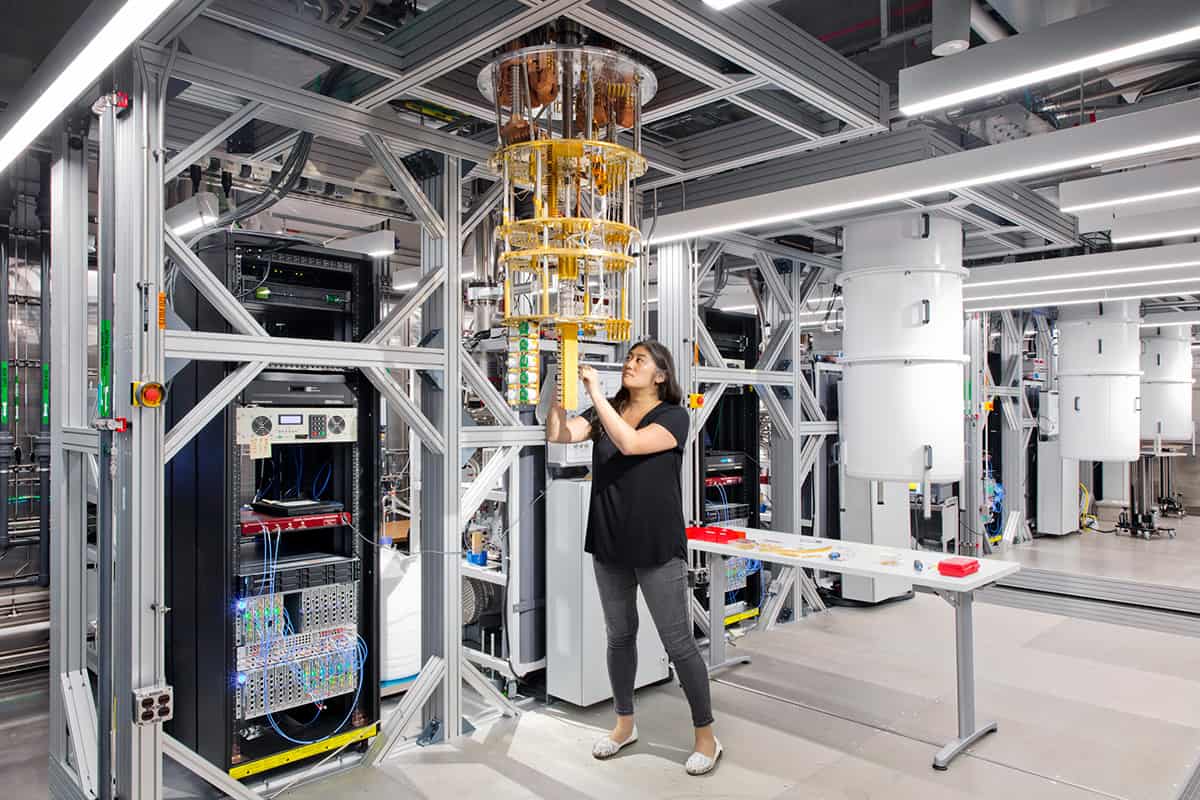 A computing laboratory with a quantum computer hanging from a metal frame and a scientist adjusting something at its base