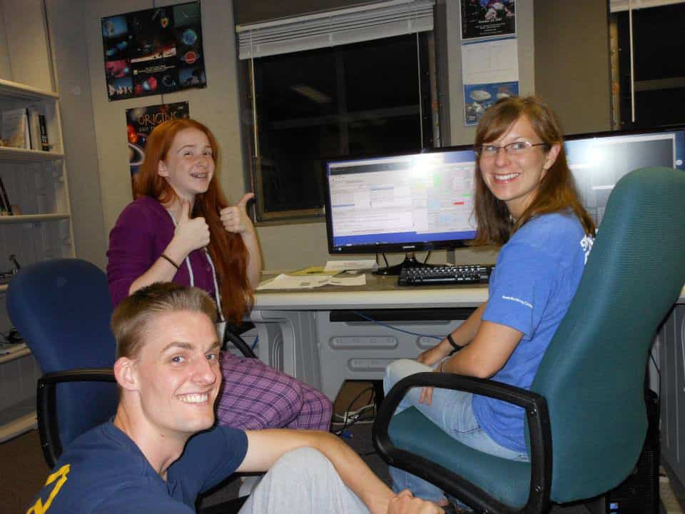 Photo of two high-schoolers and a woman looking at data on a computer screen